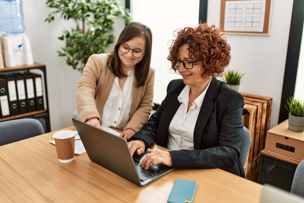 Two Women Are Sitting at a Table Looking at a Laptop Computer — Adaptive Care Pty Ltd In Tarneit, VIC