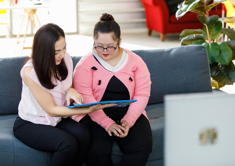 Two Women Are Sitting On A Couch Looking At A Tablet — Adaptive Care Pty Ltd In Tarneit, VIC