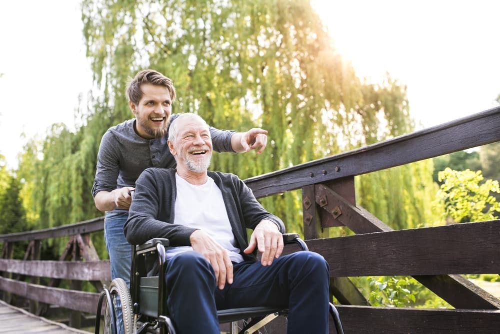 Man Pushing Another Man On A Wheelchair — Adaptive Care Pty Ltd In Tarneit, VIC