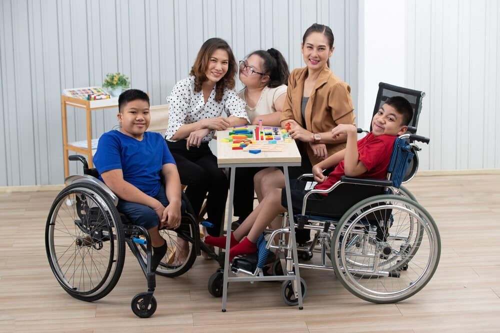 A Group of People in Wheelchairs Are Sitting Around a Table — Adaptive Care Pty Ltd In Tarneit, VIC