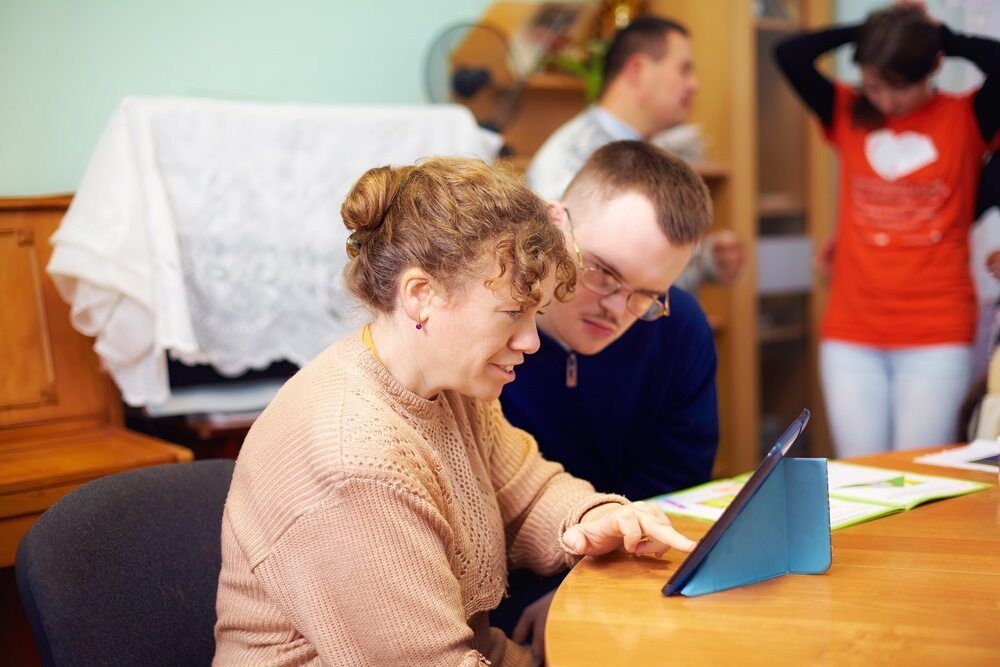 A Woman and Man Sit at a Table Engaged With a Tablet — Adaptive Care Pty Ltd In Werribee, VIC