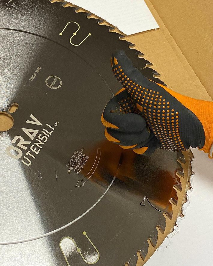 Mano guantata che impugna una lama di sega circolare su una superficie di cartone