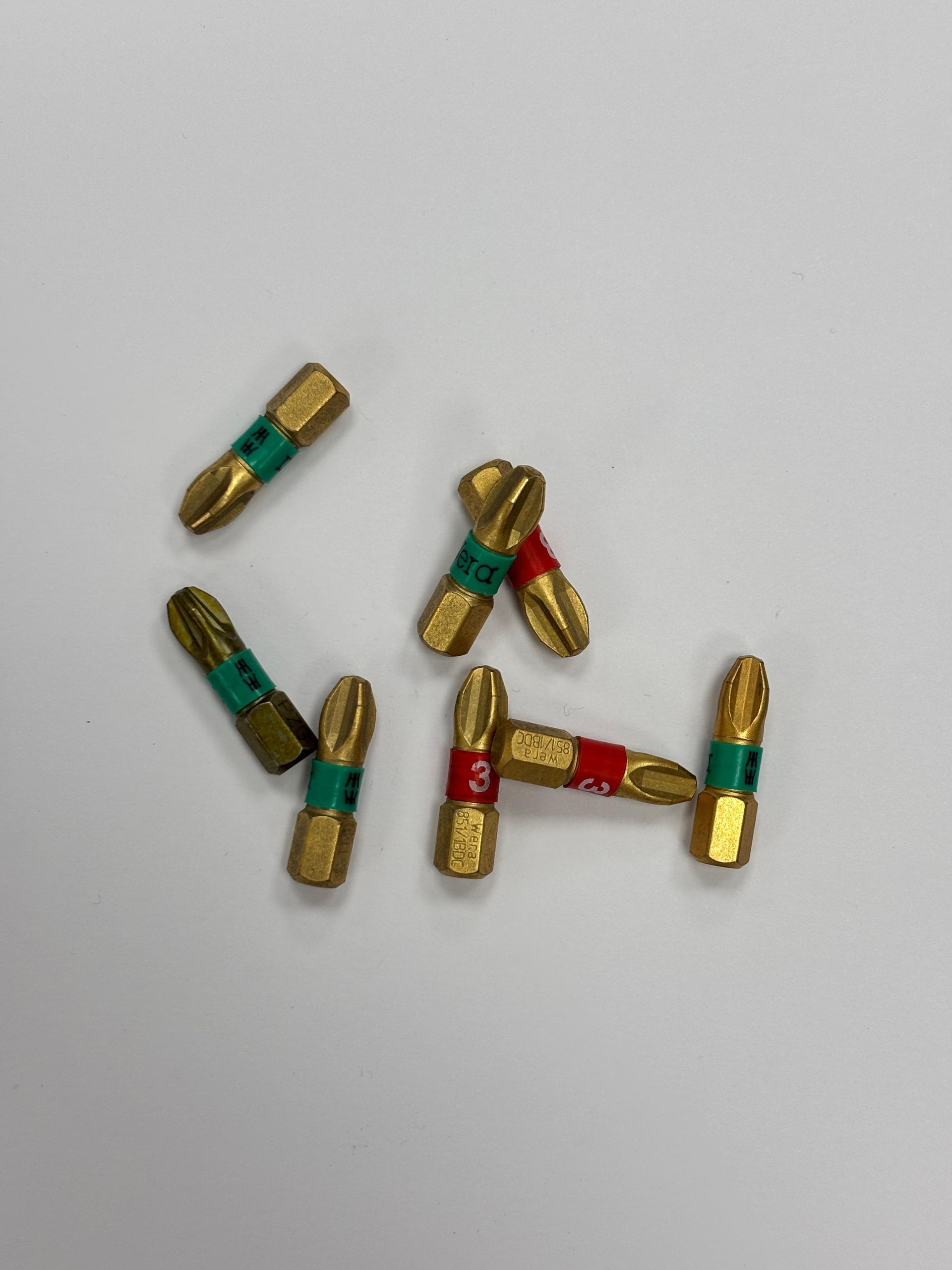 Piccoli connettori a vite color oro e verde sparsi su una superficie grigio chiaro.