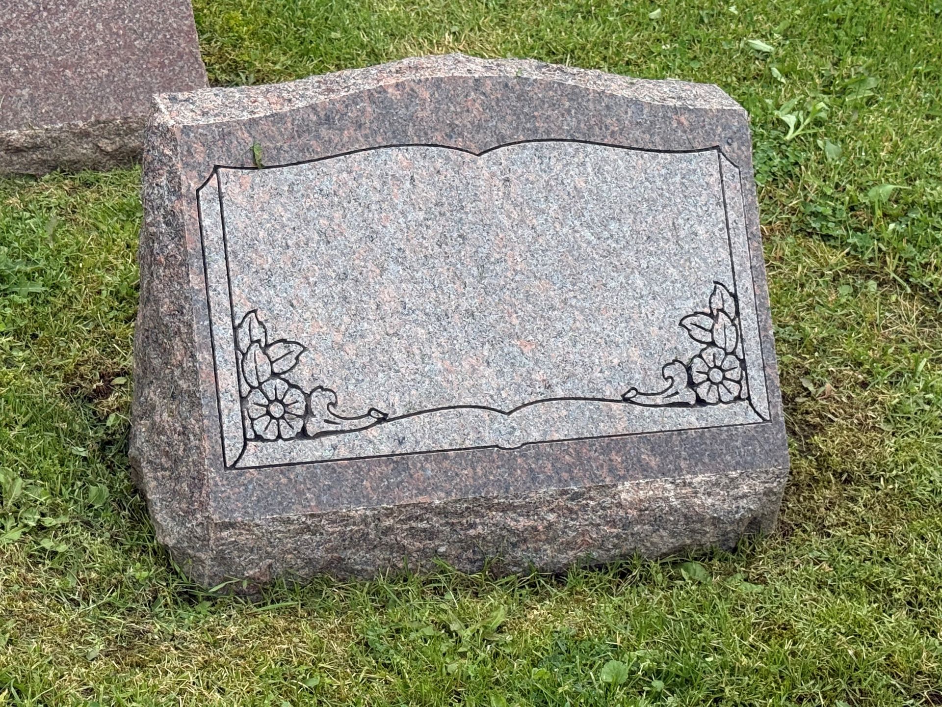A gravestone is sitting in the grass in a cemetery.