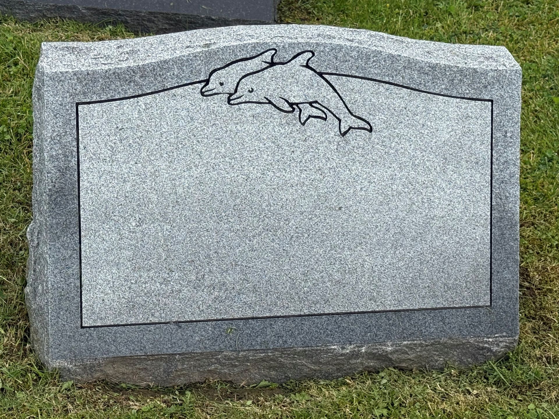 A gravestone with two dolphins carved into it is sitting in the grass.