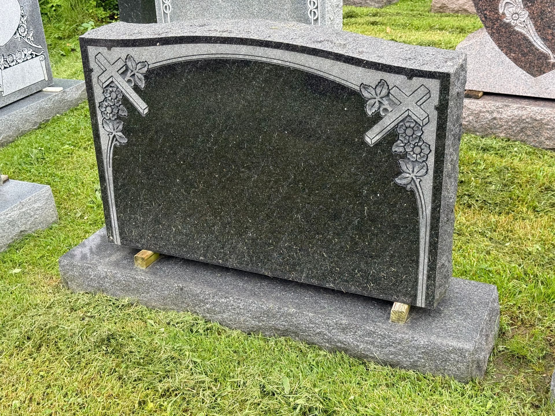 A black gravestone is sitting in the grass in a cemetery.