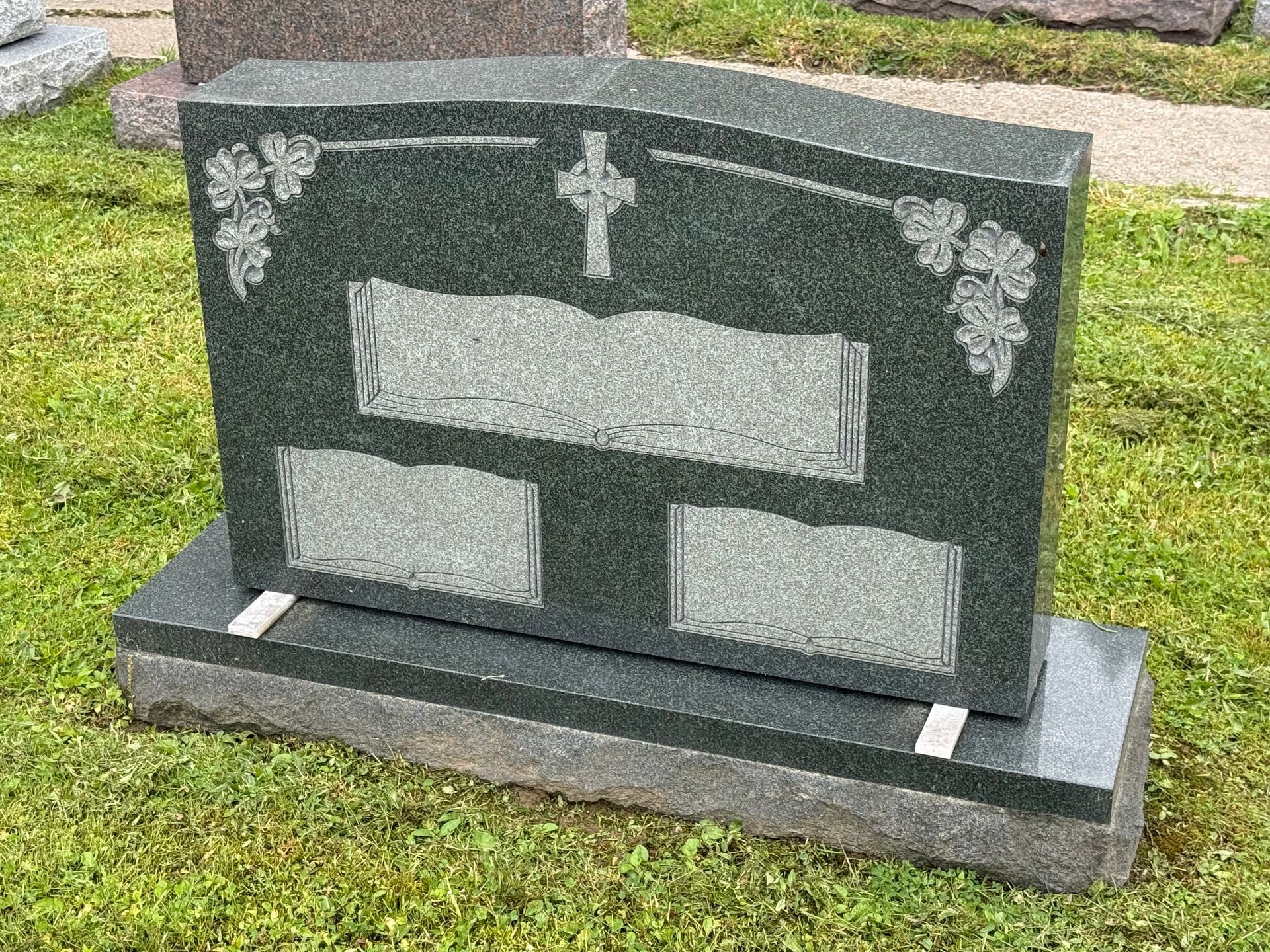 A gravestone in a cemetery with a cross and leaves on it.
