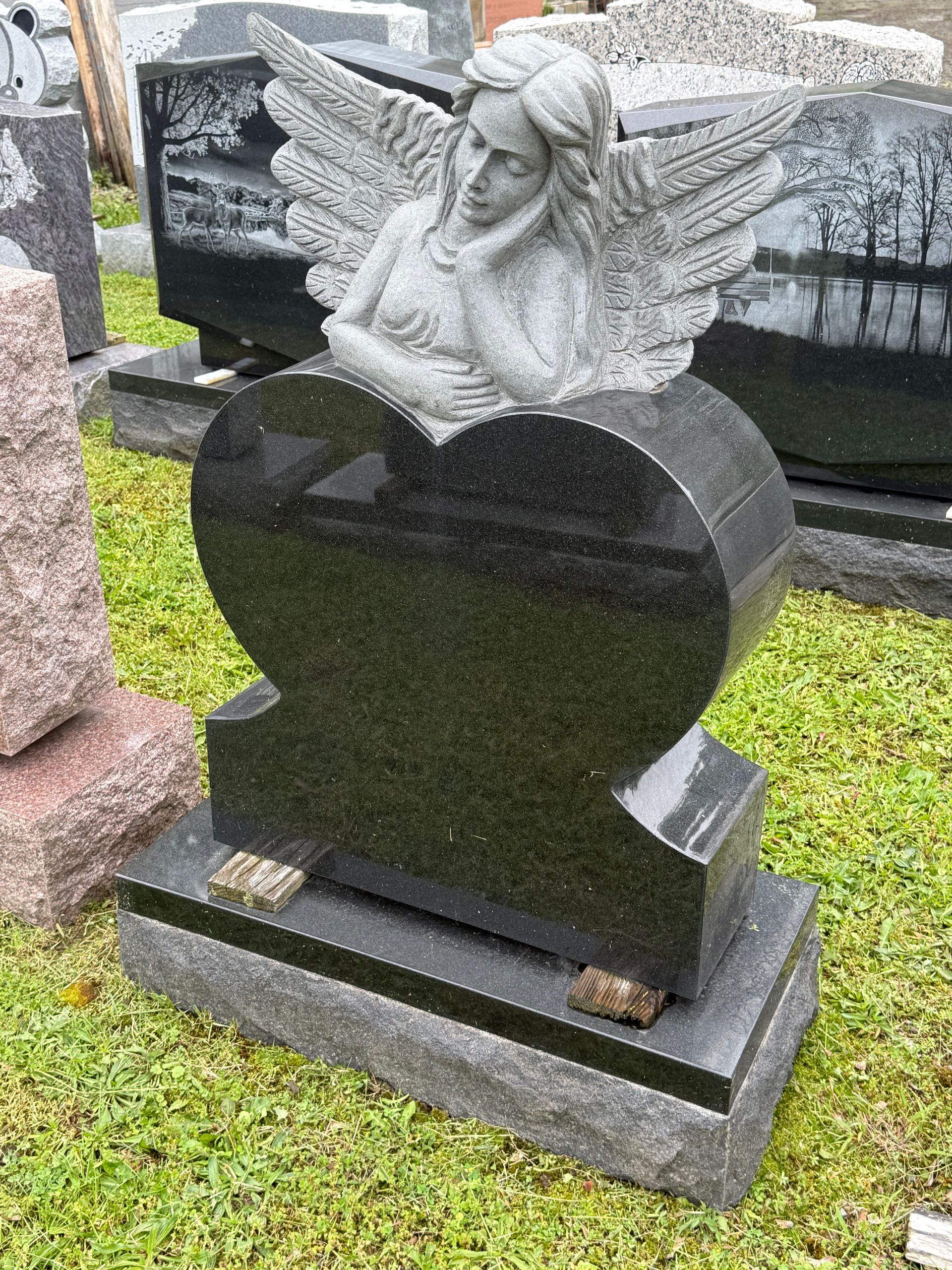 A black gravestone with a statue of an angel in the shape of a heart.