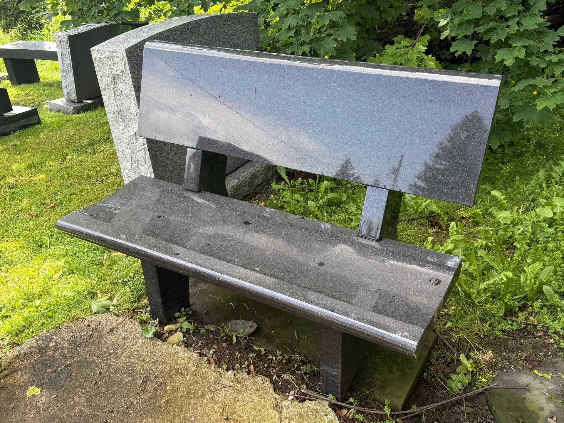 A black granite bench is sitting in the grass in a cemetery.