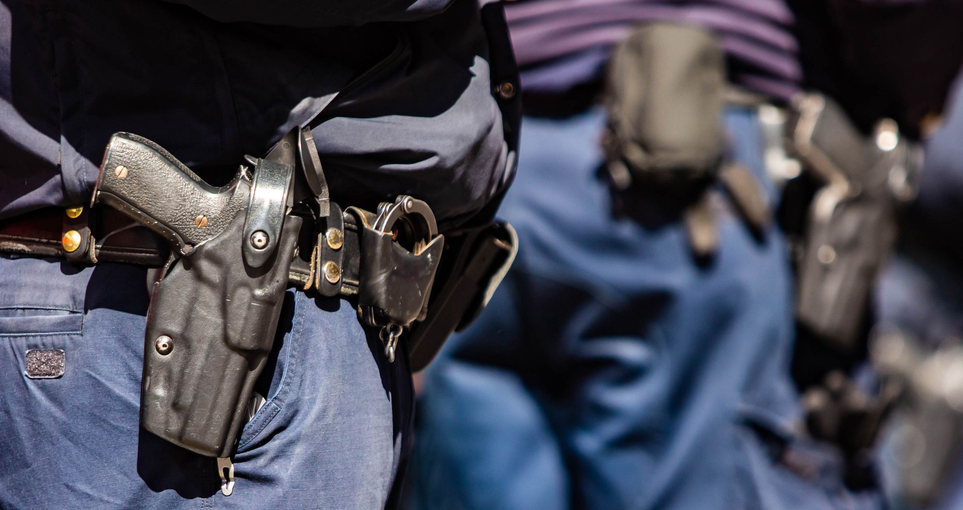 Police officers wearing duty belts with holstered firearms and handcuffs in a close-up side view.