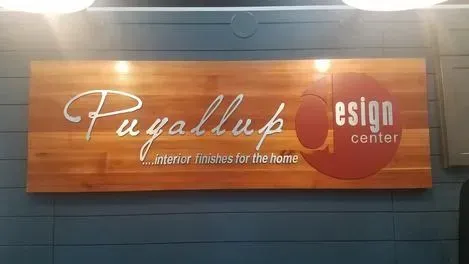 Puyallup Design Center sign on a wood panel against a dark wall with bright lights above