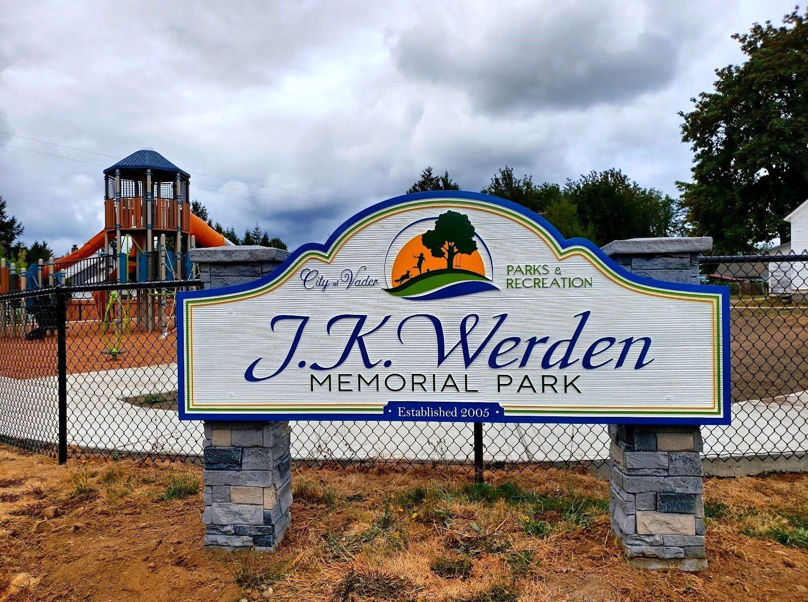 J.K. Werden Memorial Park sign in front of a playground under a cloudy sky