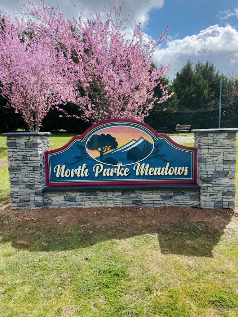 North Park Meadows entrance sign with pink flowering trees behind a stone wall.