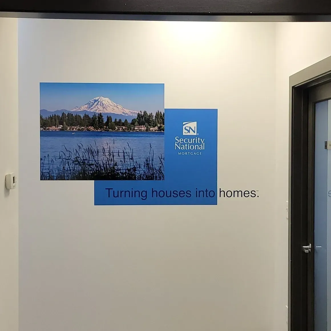 Wall sign with mountain photo and blue logo reading “Turning houses into homes” in a hallway
