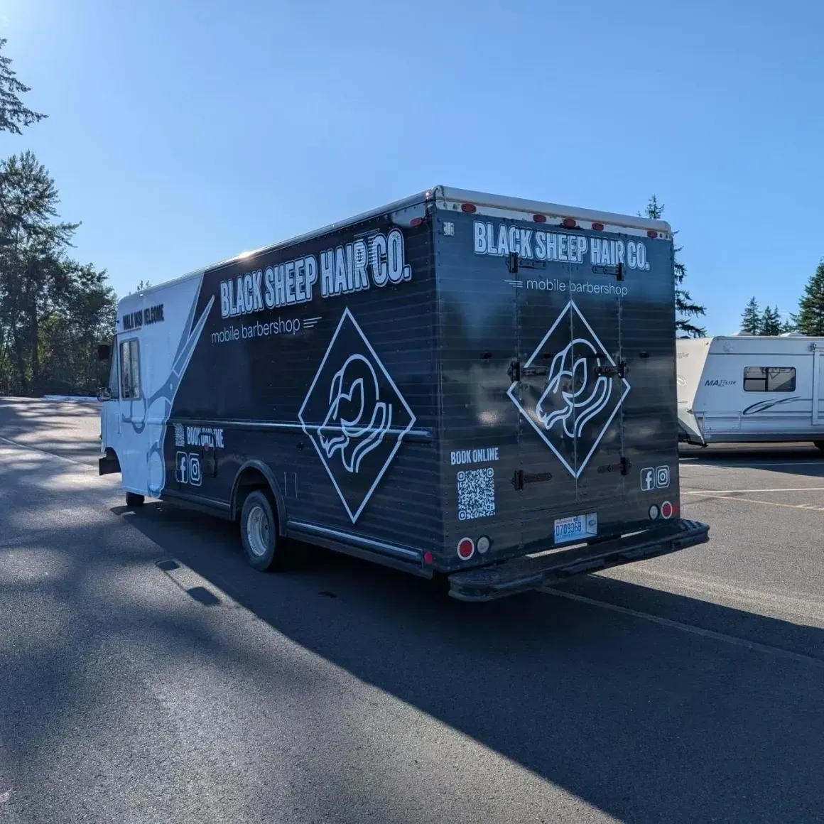 Dark wrapped food truck parked on a sunny street, labeled “BLACK SHEEP BURGER CO.”
