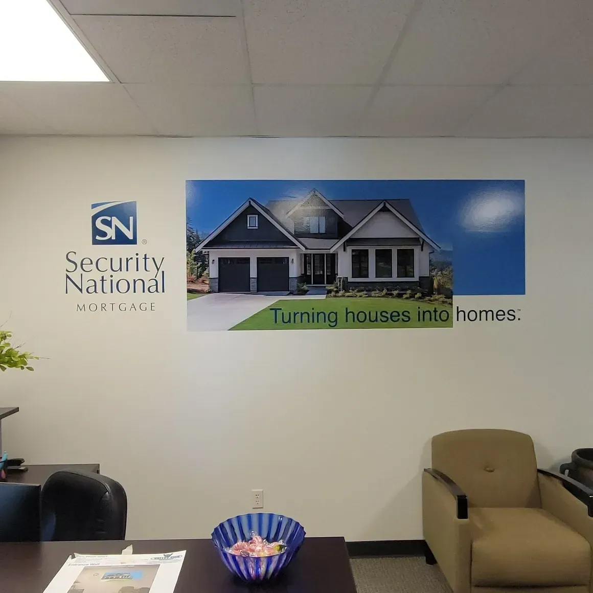 Office waiting room with Security National sign, house poster, chair, and bowl of candy on a table