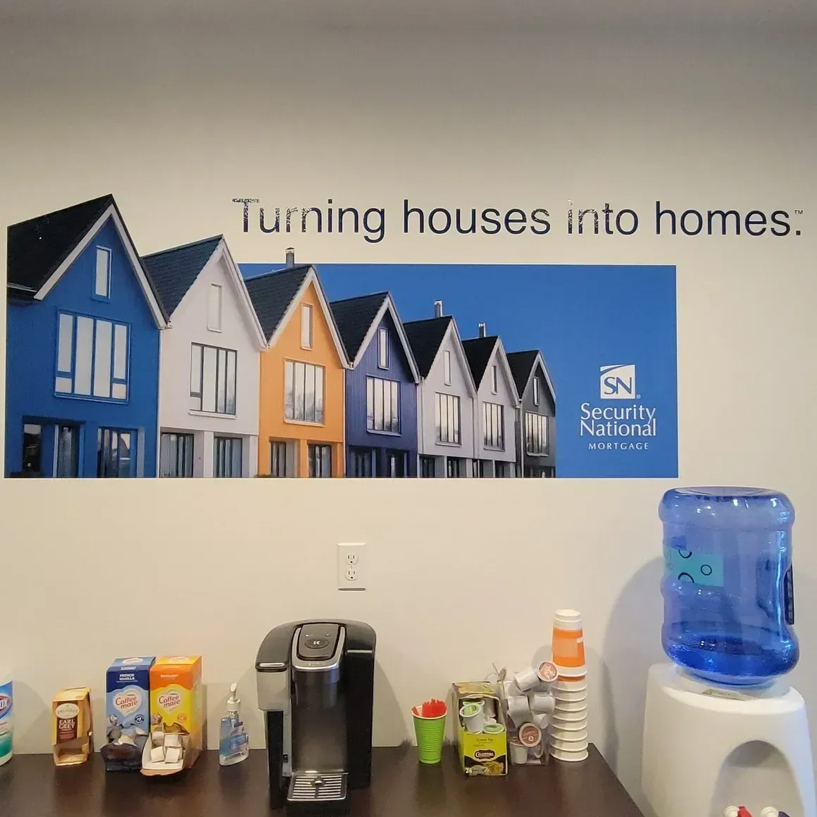 Office wall with “Turning houses into homes” banner, coffee station, and water cooler.
