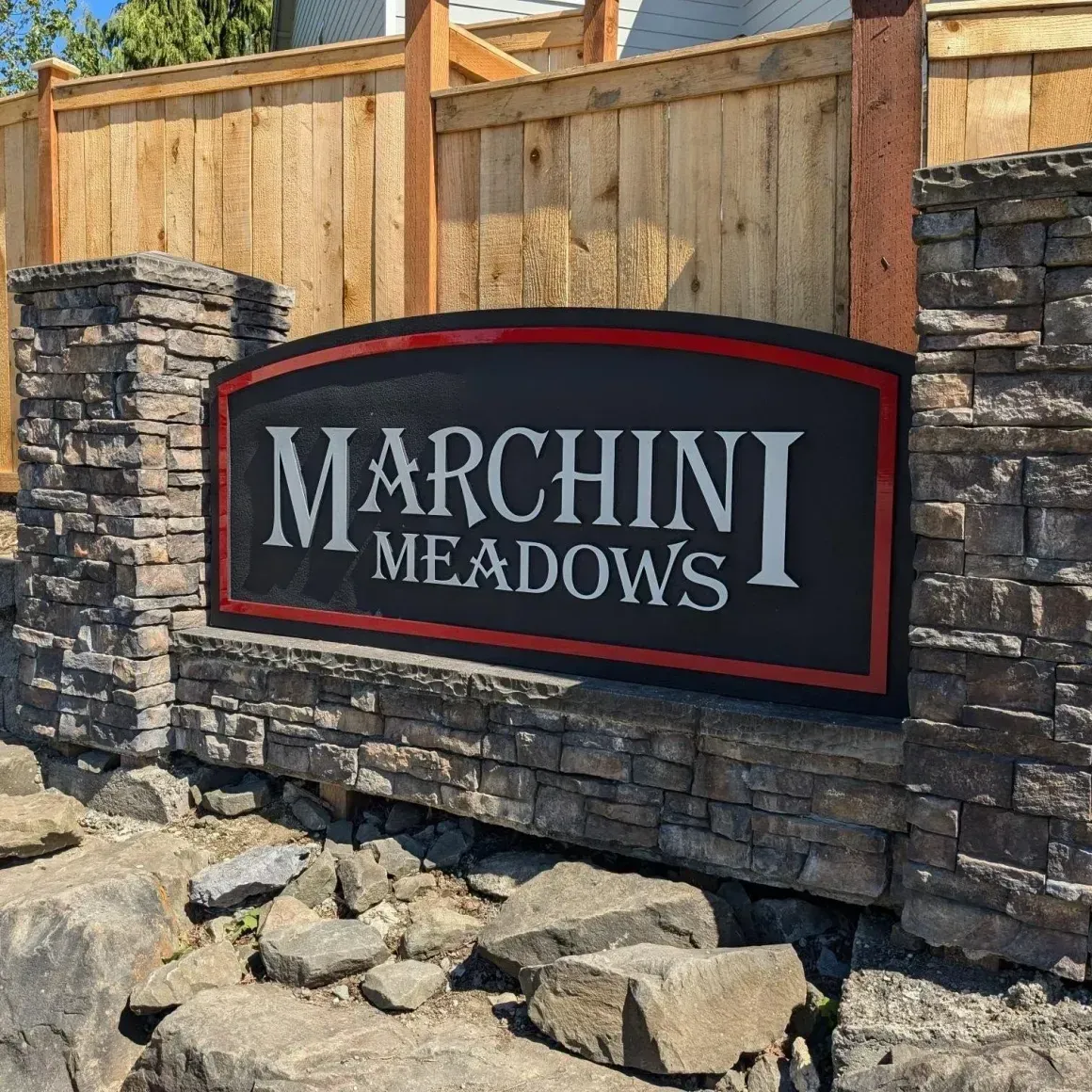 “Marchini Meadows” sign on a stone wall with a wooden fence behind it created by Valley Sign