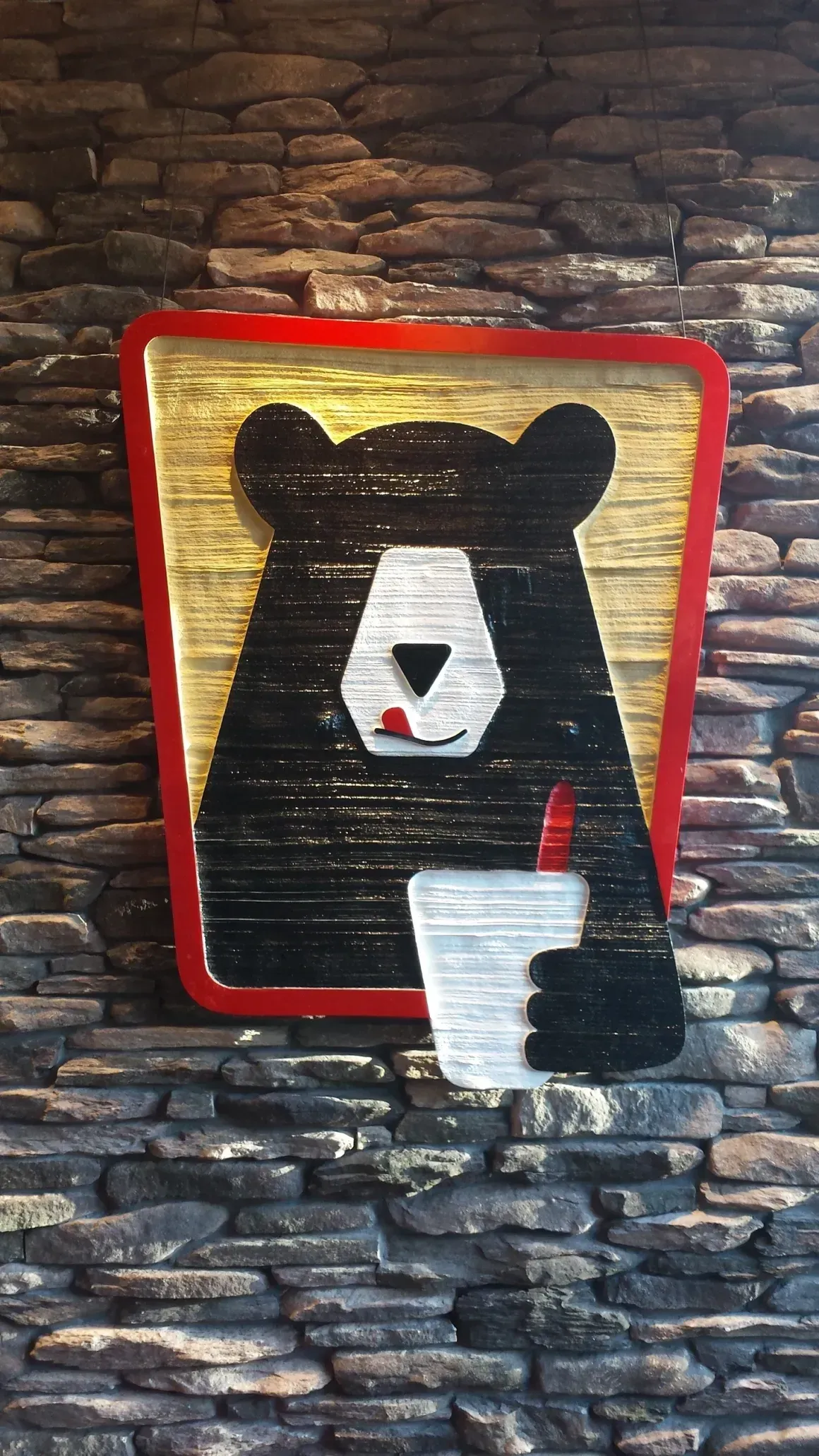 Black bear logo on a stone wall inside a red-outlined square, holding a white cup.