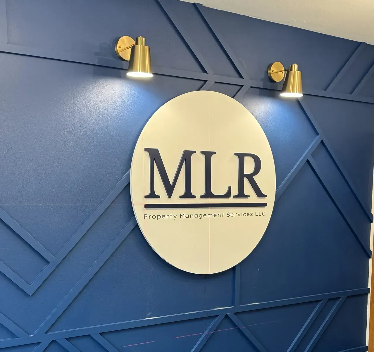 Gold MLR logo sign on a blue geometric wall with small lights above