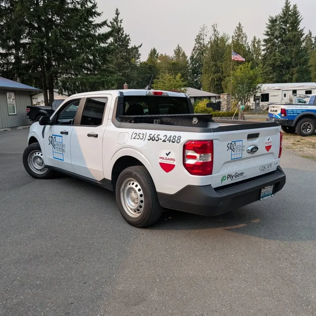 White utility pickup truck parked outdoors near trees and buildings, with company decals and phone number on the side