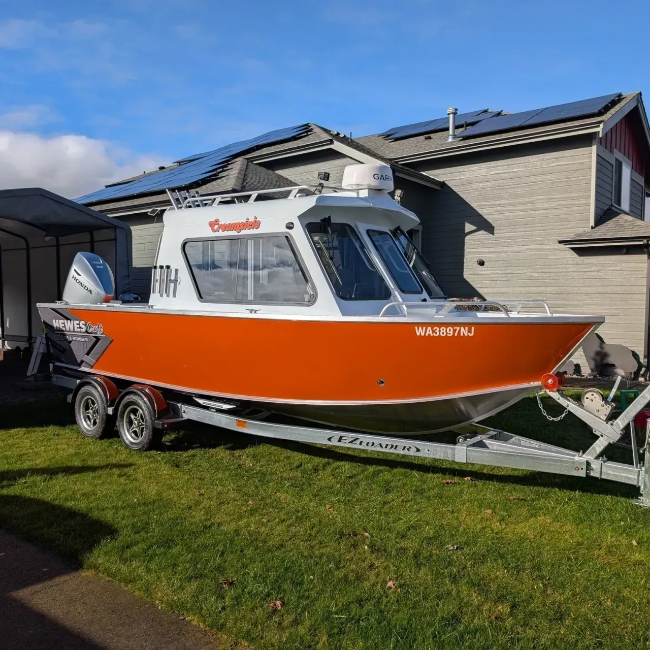 Orange-and-white cabin fishing boat on a trailer parked on a grassy driveway beside a house.