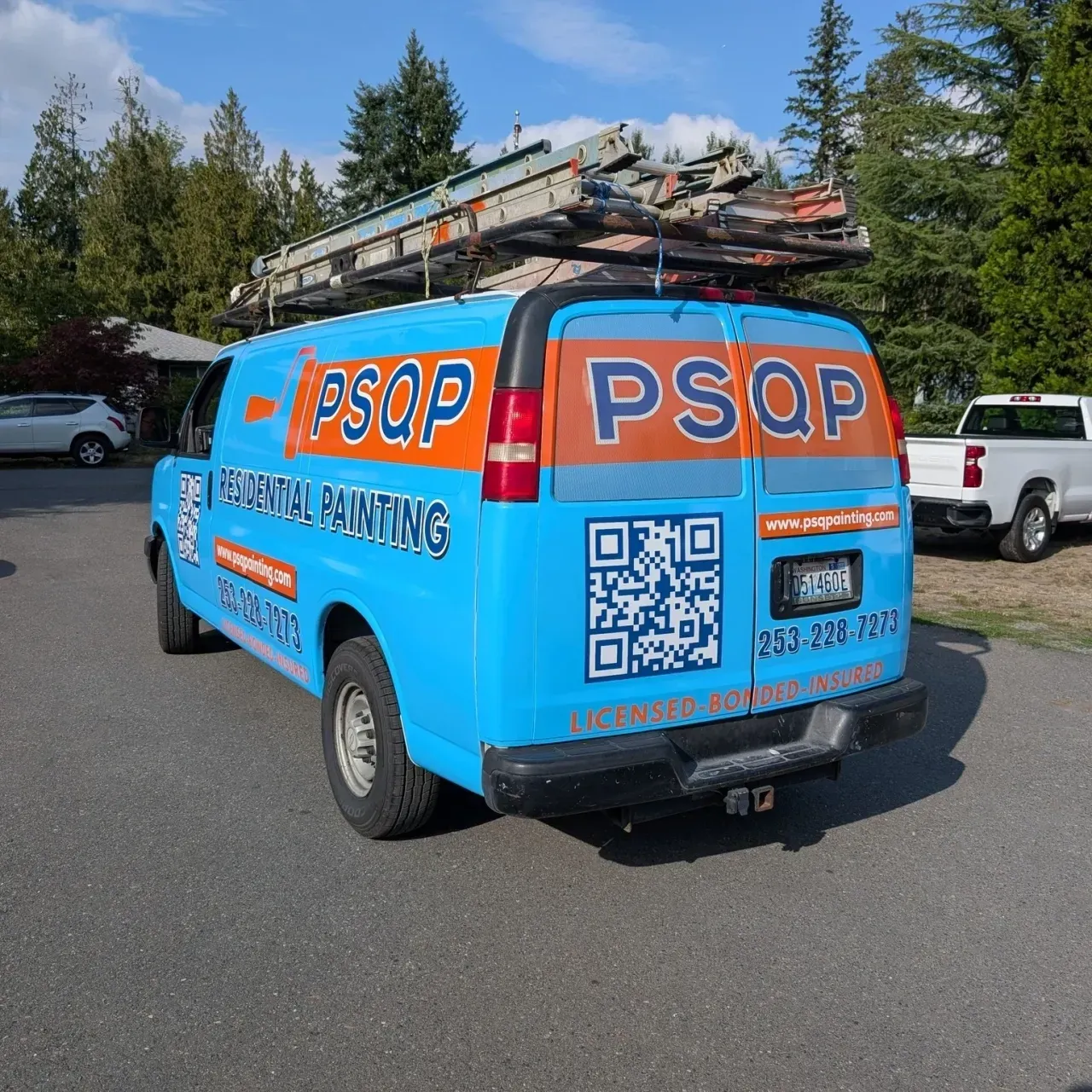 Bright blue PSQP service van with ladders on top, parked outdoors on a sunny street.