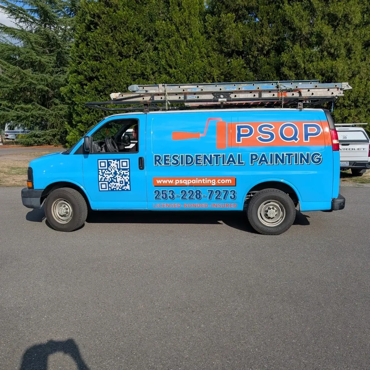 Bright blue residential painting van with ladder on top, parked on a street.