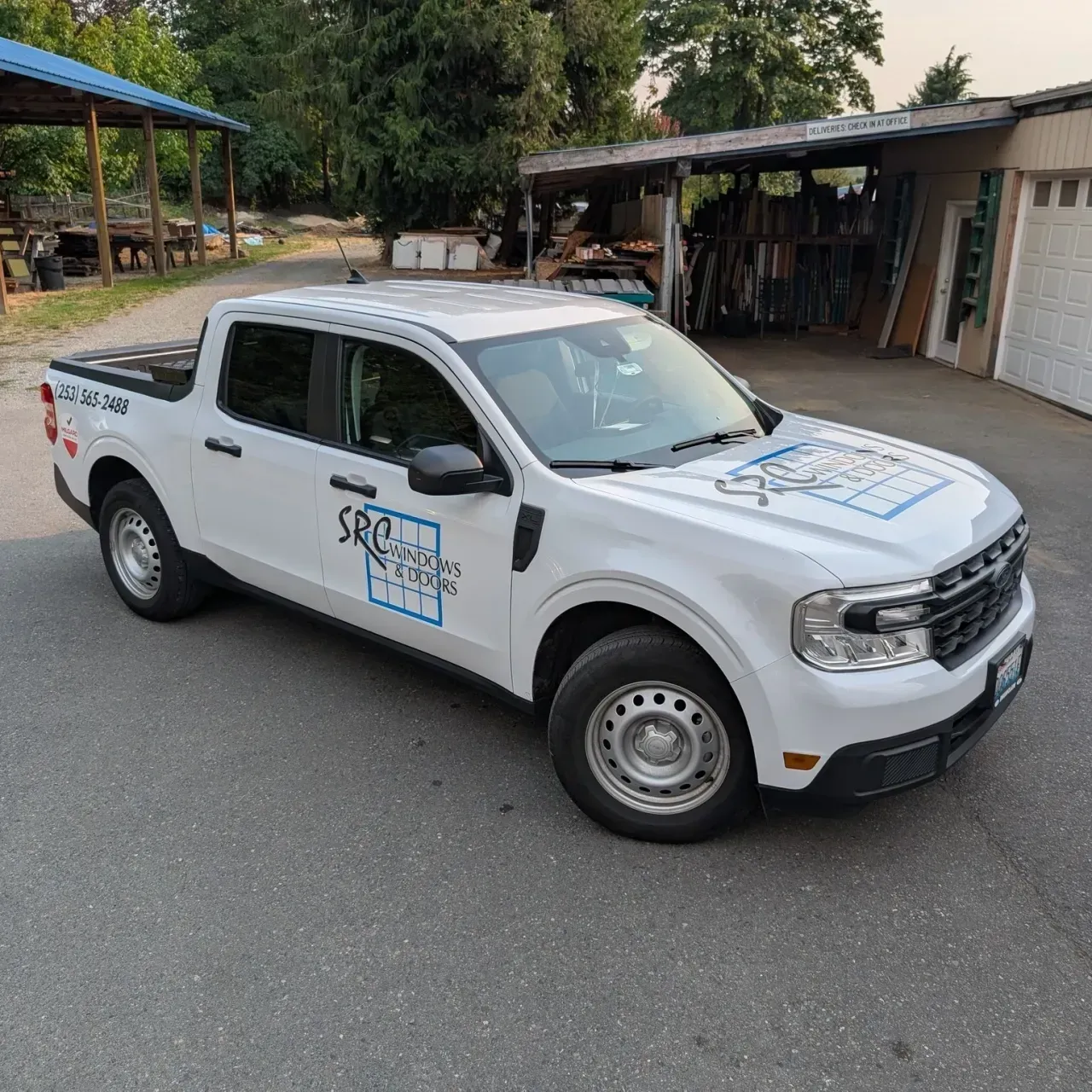 White pickup truck with blue logo decals parked on a roadside near a building.