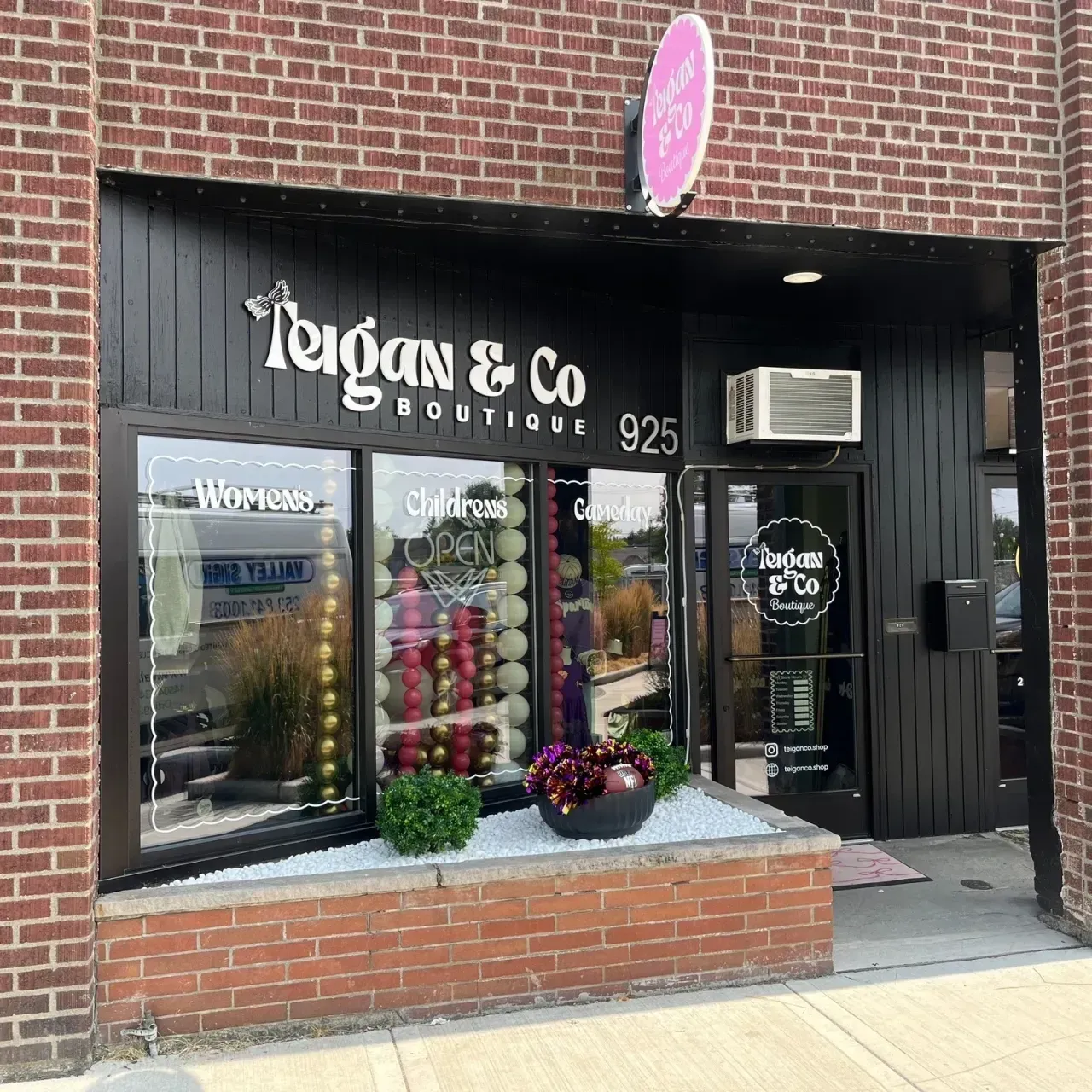 Storefront of Logan & Co Boutique with black facade, brick planter, and clothing displays in the windows