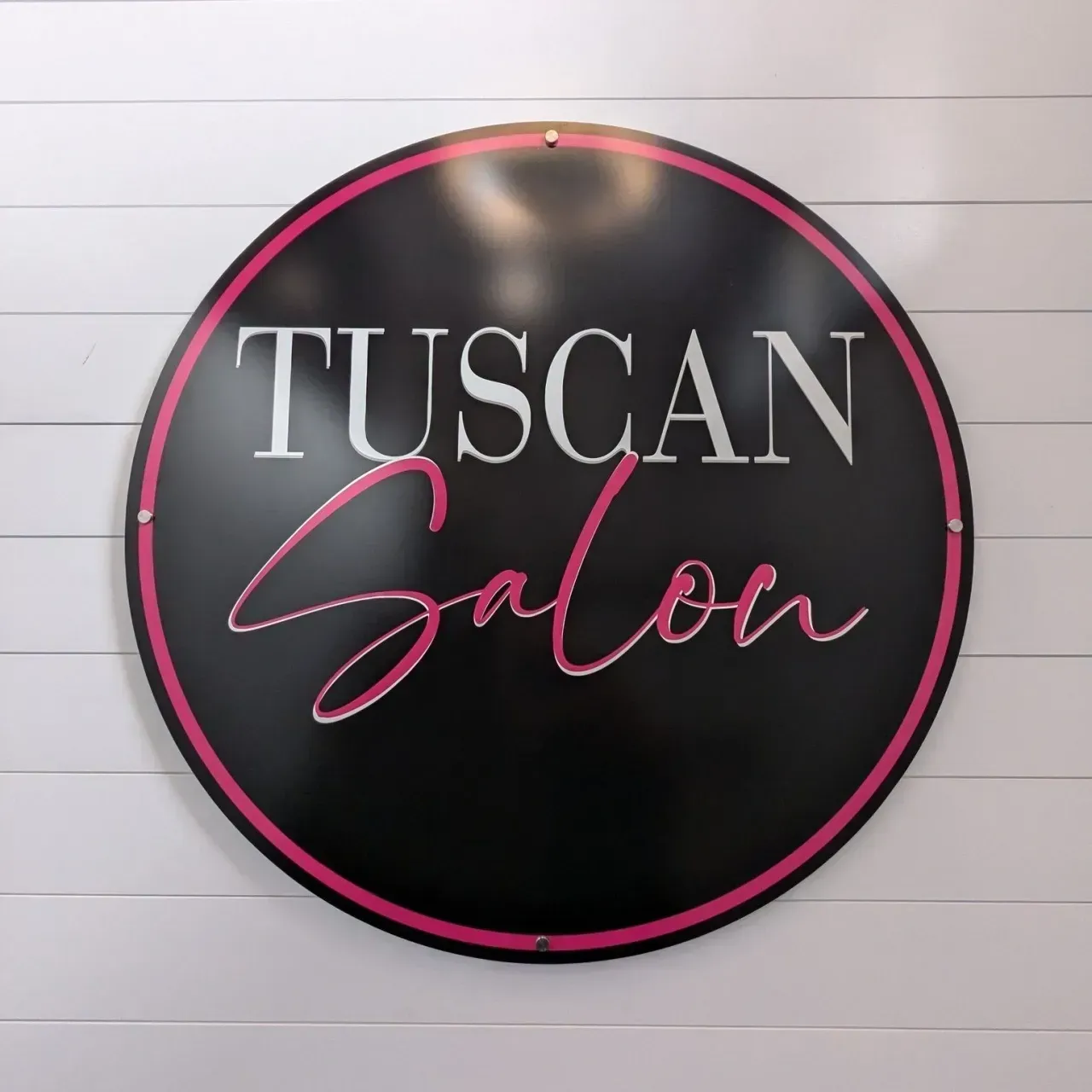 Tuscan Salon logo on a black circular sign with pink script and trim