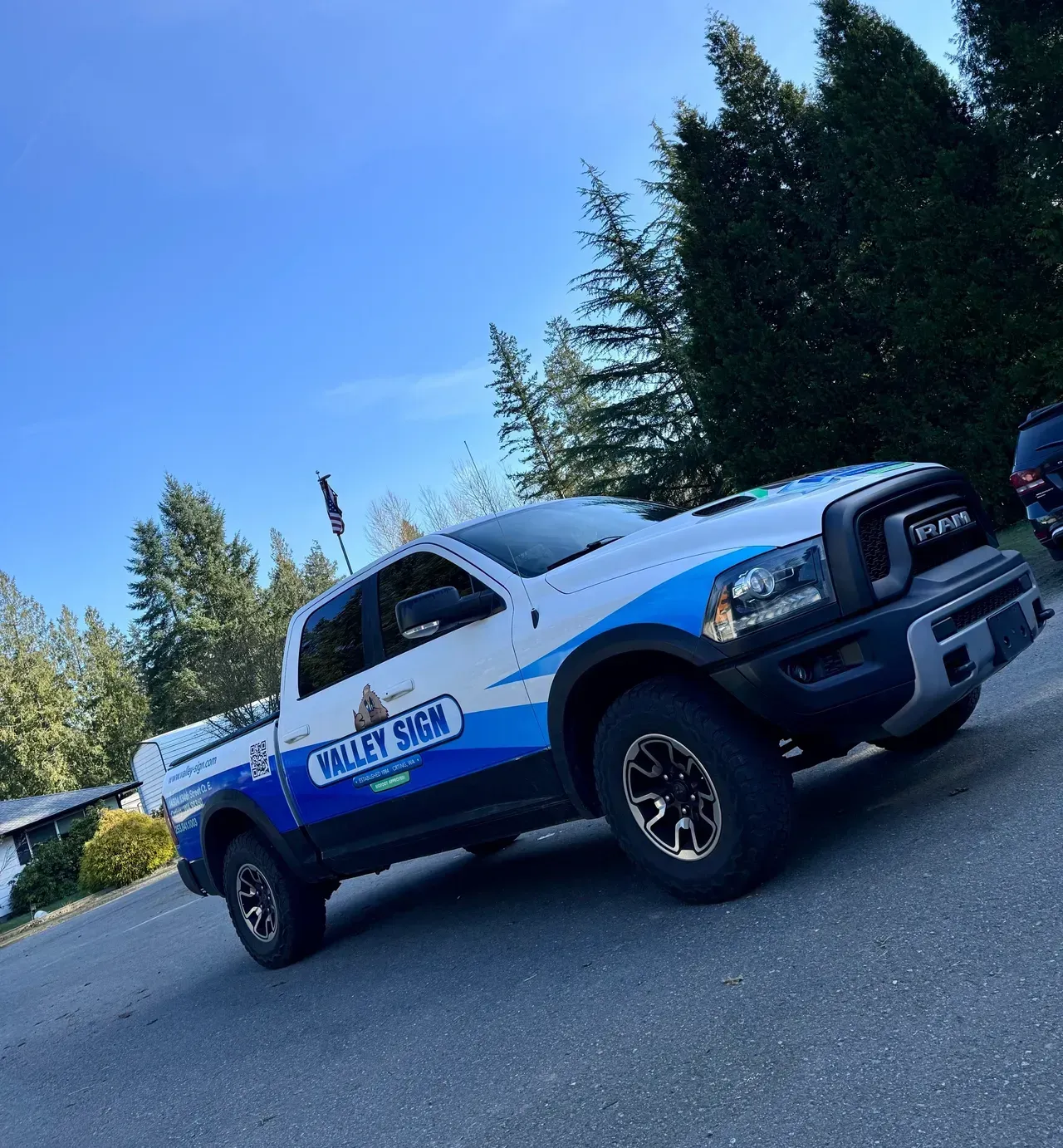 White and blue pickup truck on a driveway with trees and blue sky in the background