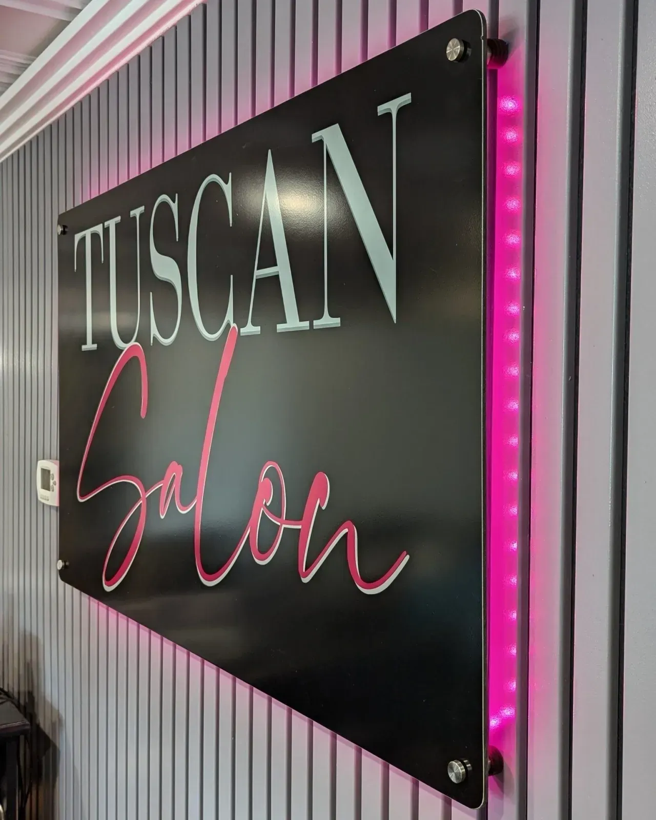 Black “TUSCAN Salon” sign with pink neon script on a striped wall