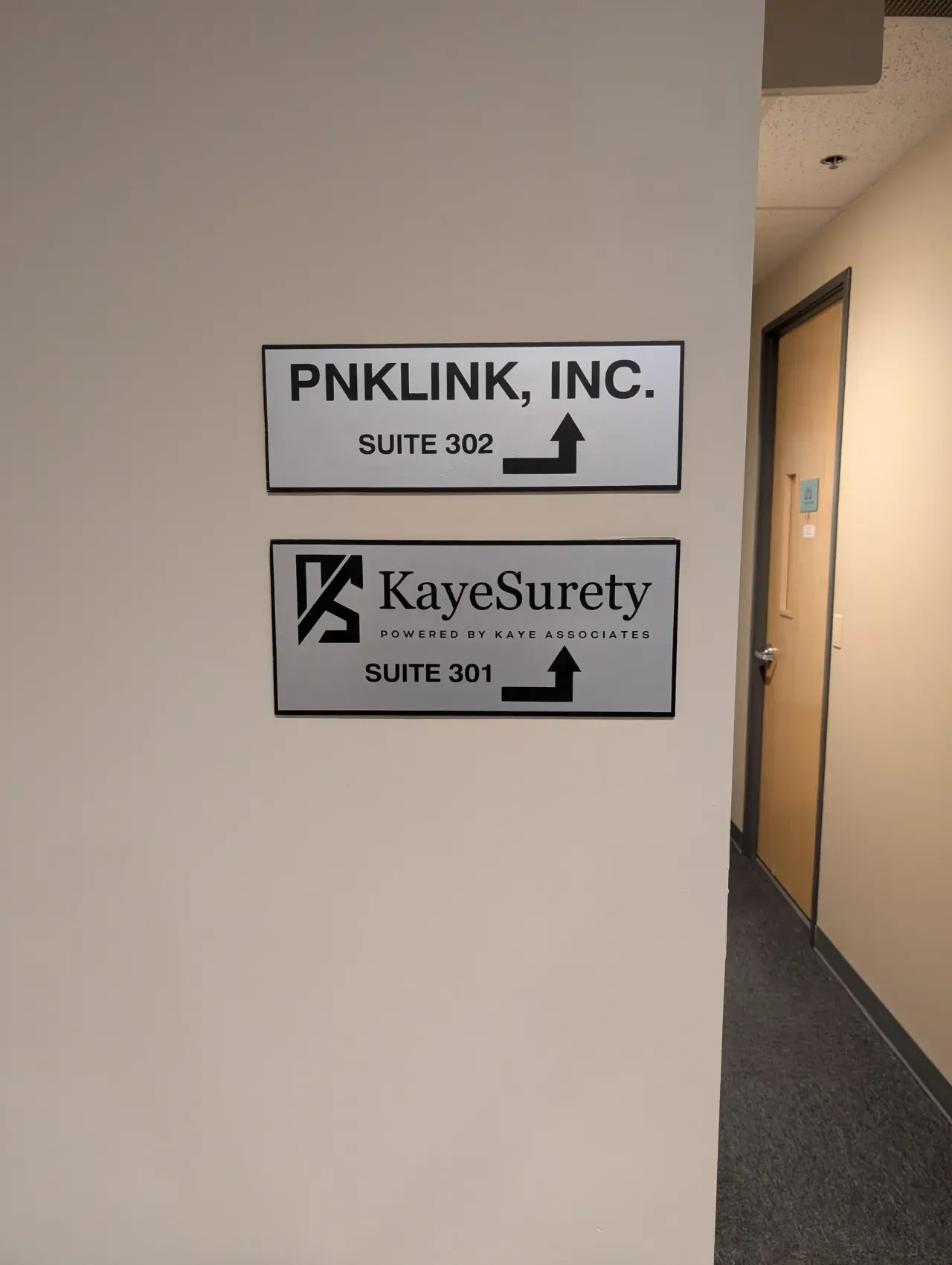 Hallway wall signs for PNKLINK, Inc. and KayeSurety with arrows pointing right