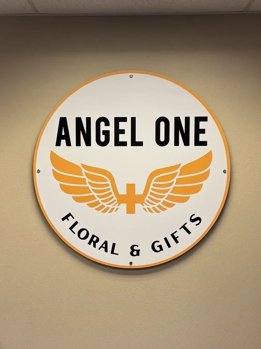 Round “Angel One Floral & Gifts” sign in black and orange on a beige wall.
