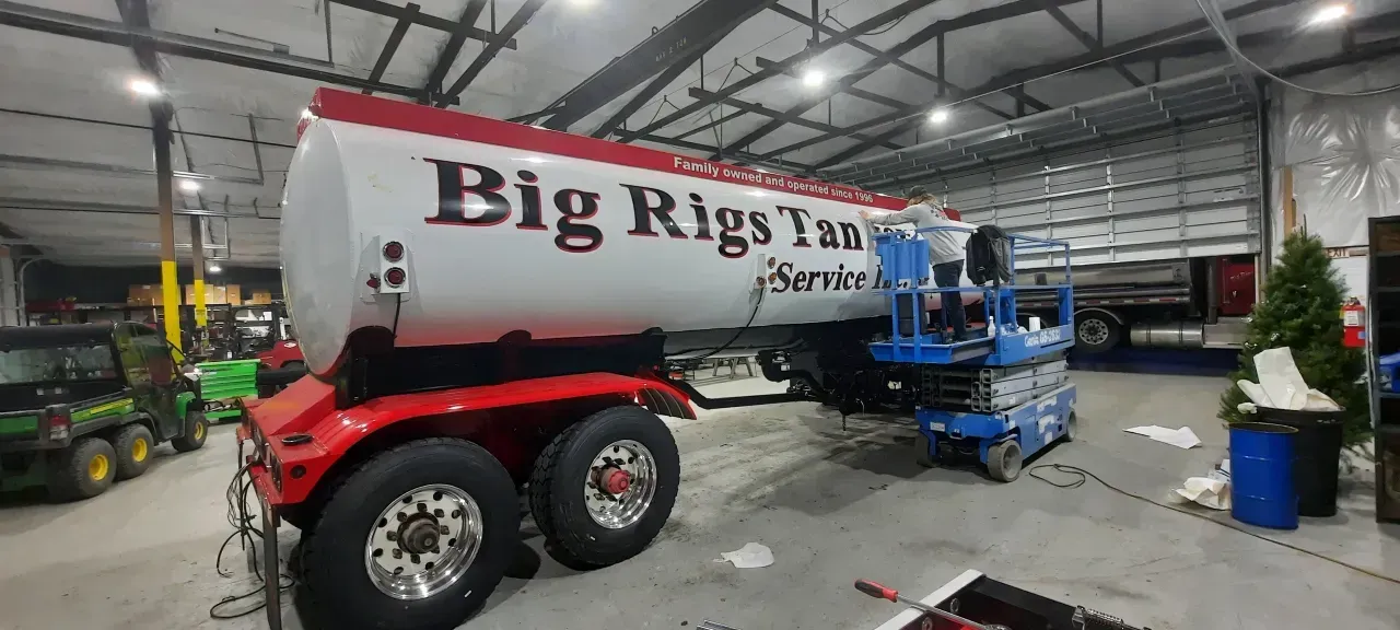 Big Rig Tank Service tanker trailer in warehouse, with blue lift equipment and a green tractor nearby