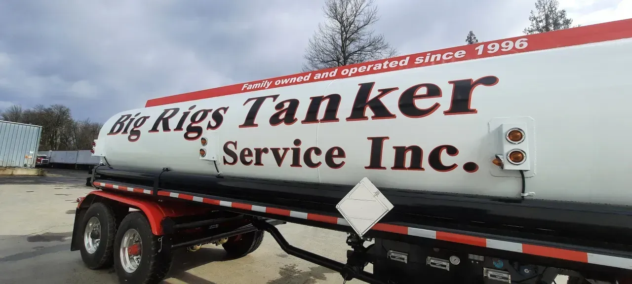 White tanker truck with “Big Rig’s Tanker Service Inc.” logo parked outdoors under a cloudy sky