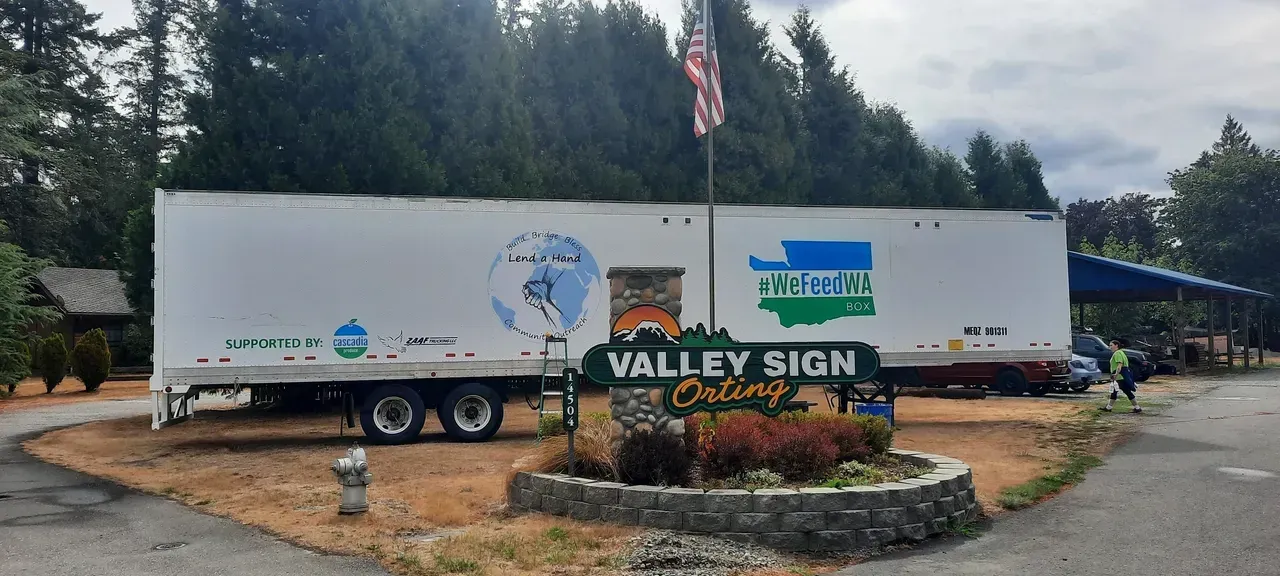 Two white Valley Sign trucks parked behind a landscaped company sign and American flag.