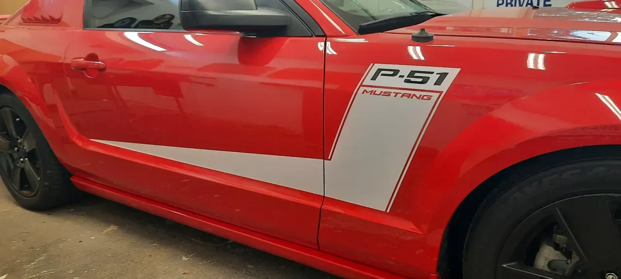 Red sports car side view with white racing stripes and black wheels in a garage.