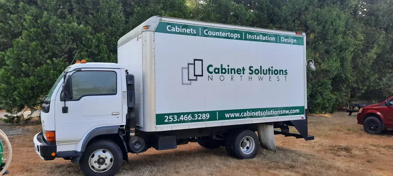 White Cabinet Solutions delivery truck parked outdoors on a dirt roadside with trees in the background