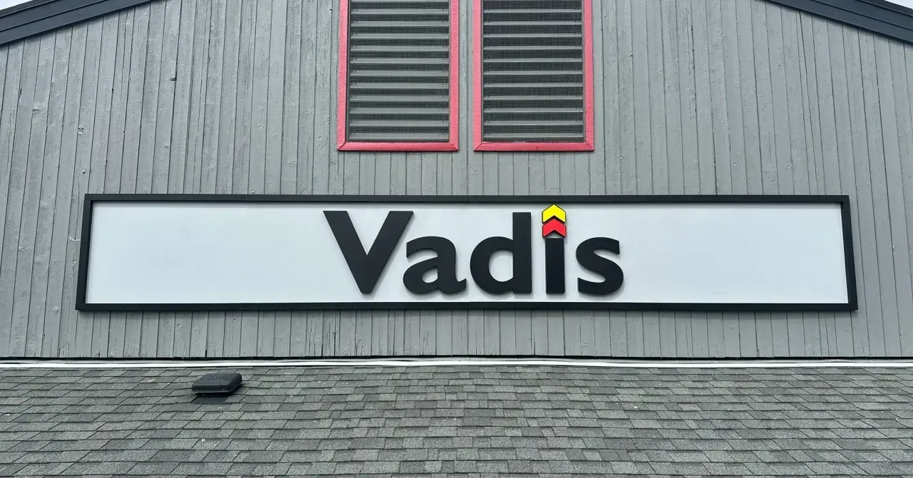 Building sign reading “Vadis” on a gray exterior wall with red-trimmed windows above.