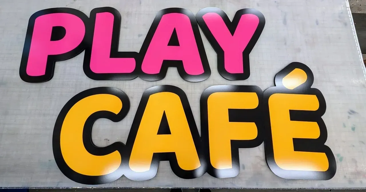 Pink and yellow “PLAY CAFE” sign on a gray wall