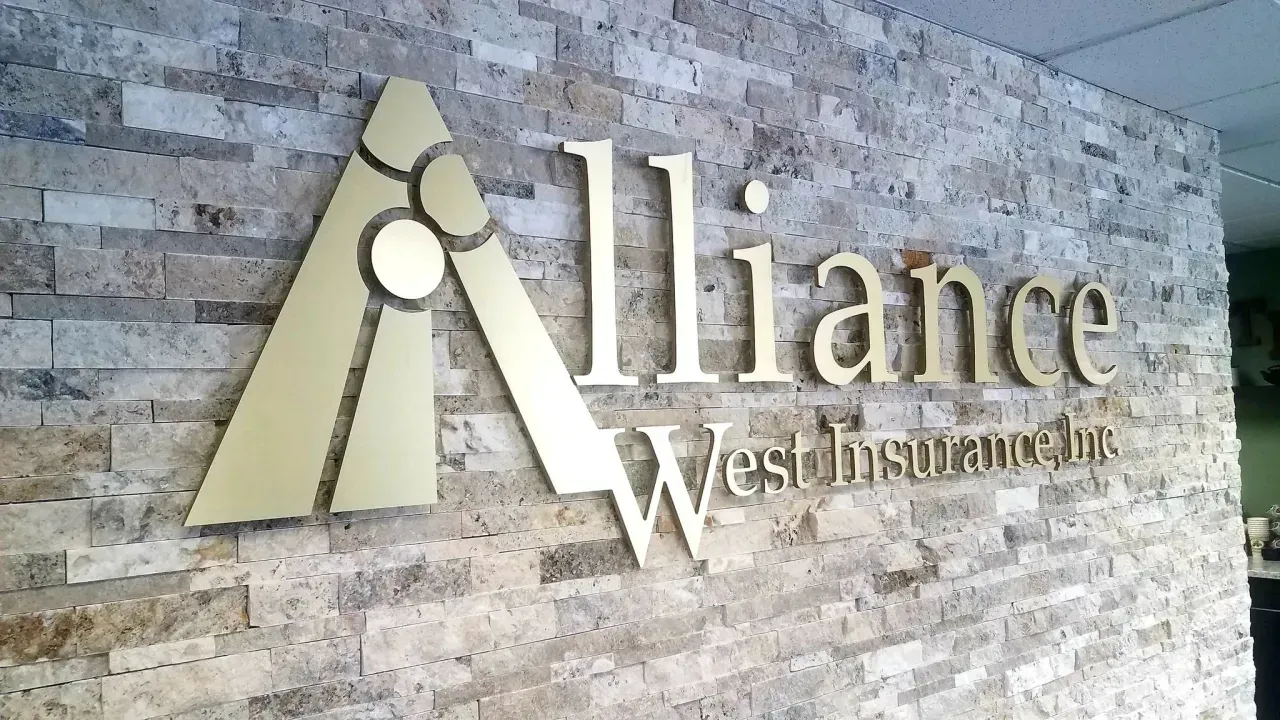 Alliance West Insurance sign on a stone wall with gold lettering and logo.
