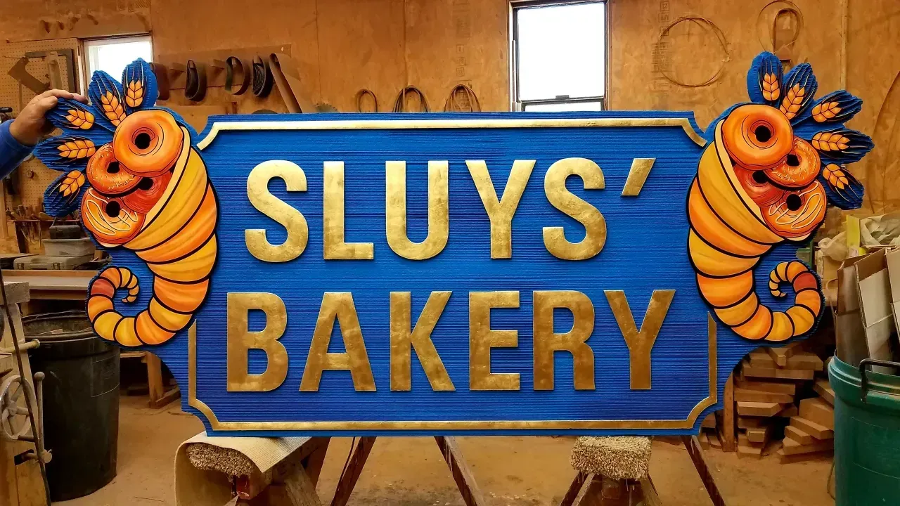 Blue sign reading “SLUYS’ BAKERY” with orange pastry decorations in a bakery interior