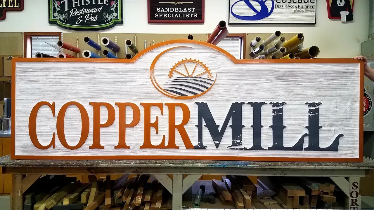 Copper Mill sign with white background, orange lettering, and a sunburst design above the text.