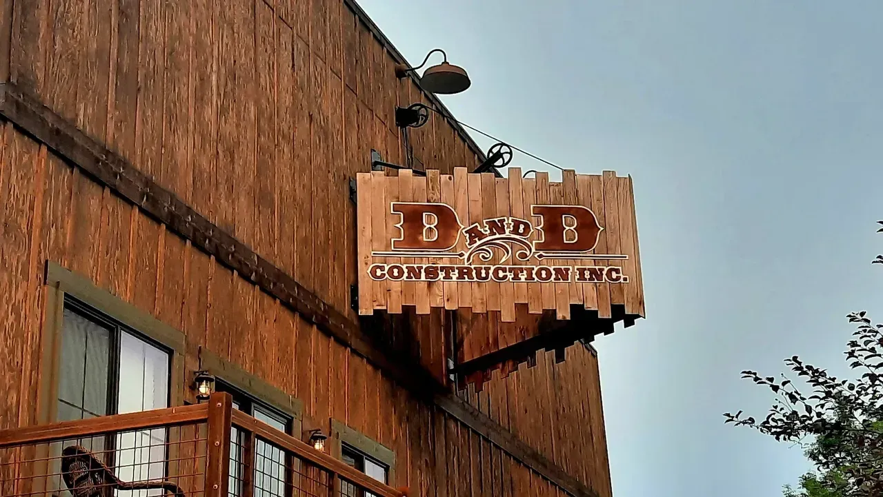 Wooden storefront sign on a rustic building under a blue sky, with hanging lamp and windows below.