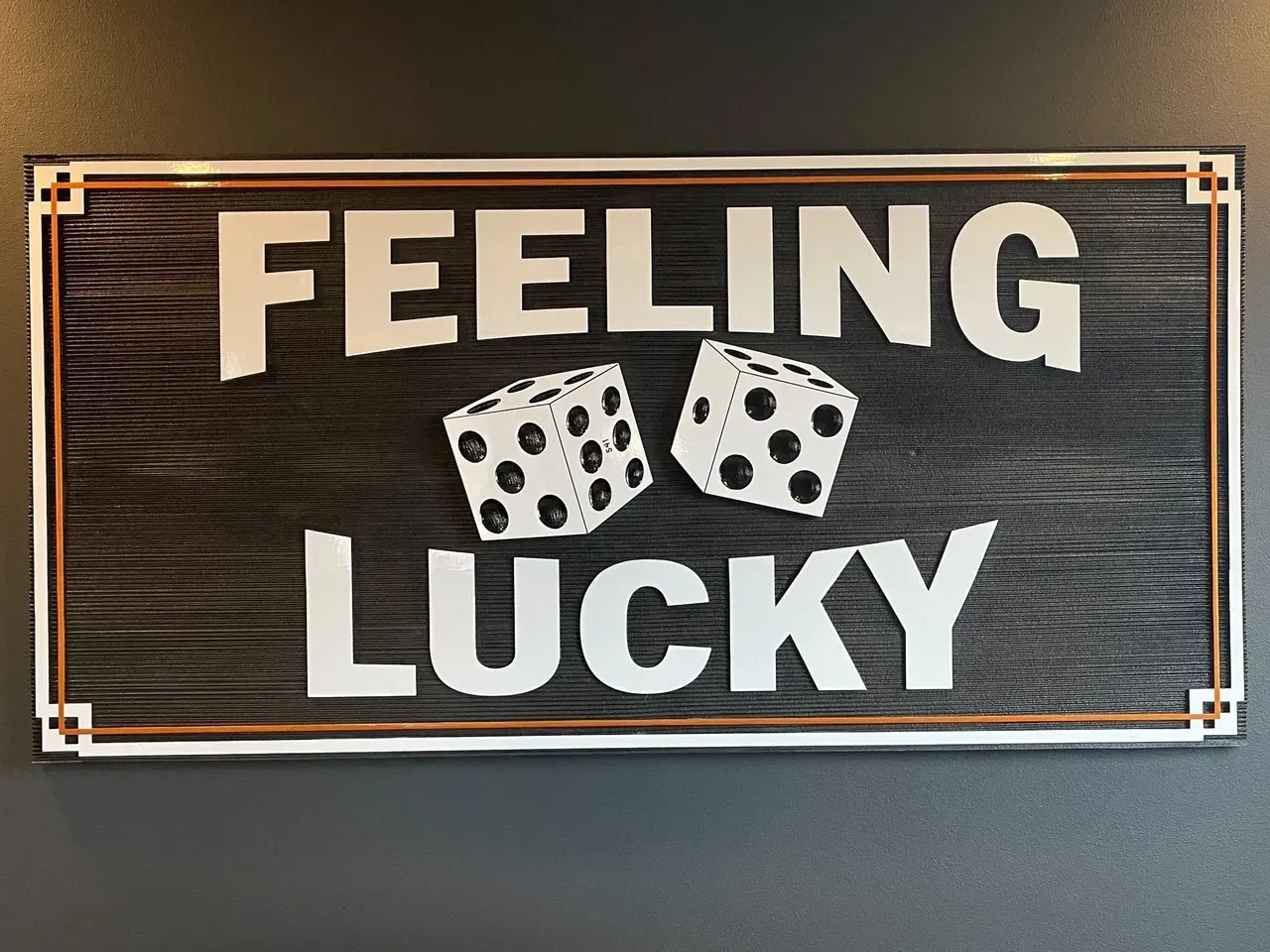 Black sign with white text “FEELING LUCKY” and two dice, framed in gold wood-like trim.