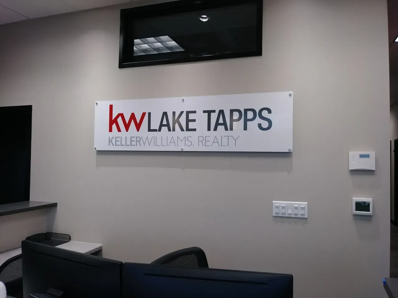 Wall sign for KW Lake Tapps Keller Williams Realty in a beige office lobby