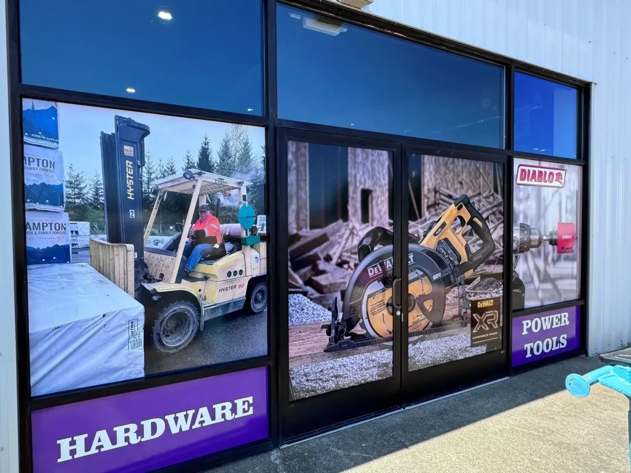 Hardware store windows with forklift and excavator graphics, plus signs reading “HARDWARE” and “POWER TOOLS”