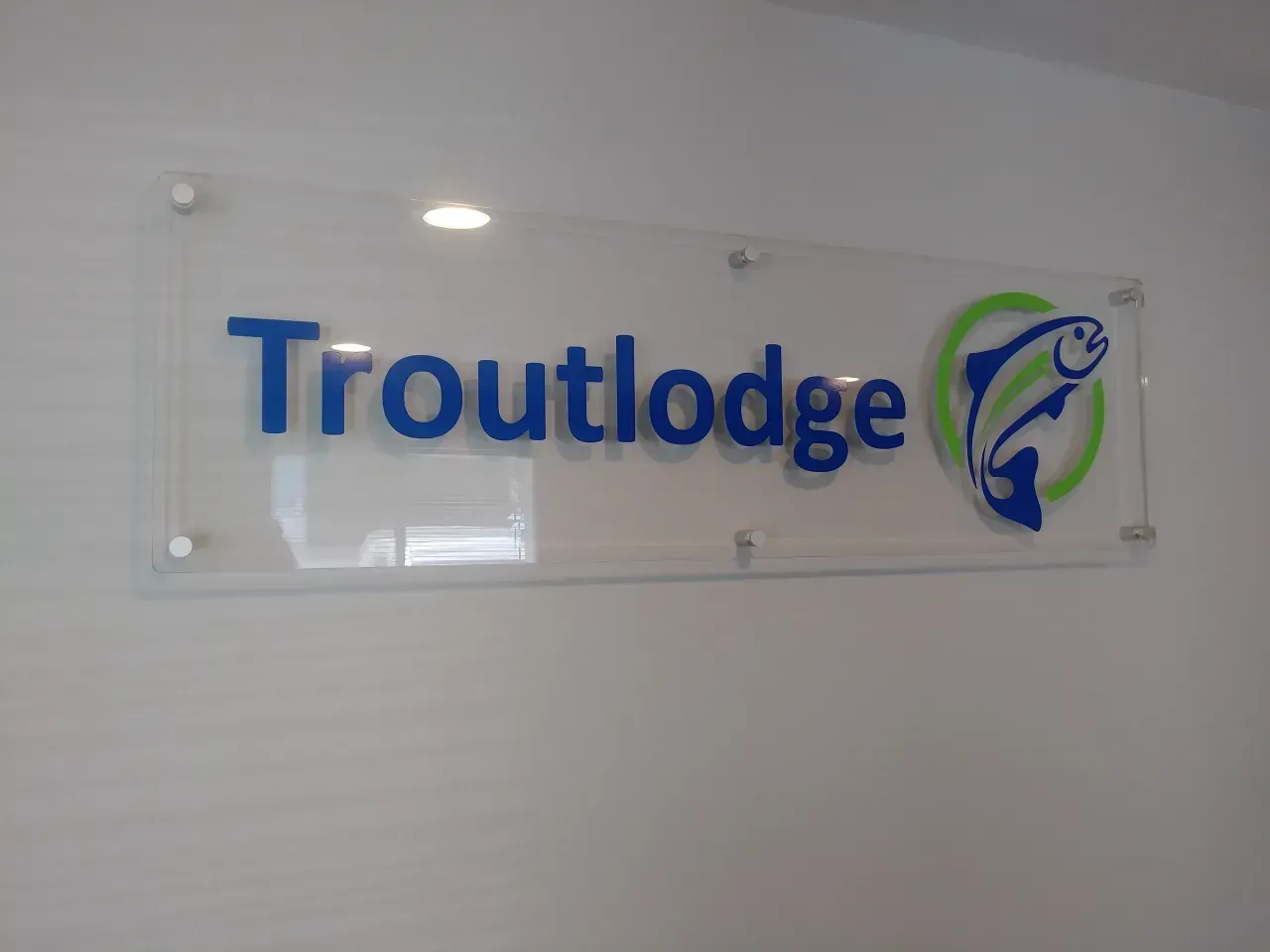 Troutlodge logo on a white wall plaque with blue text and a fish icon